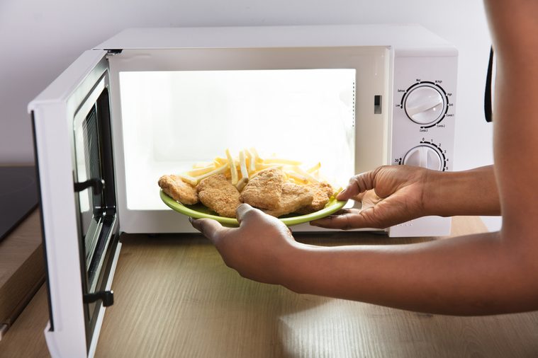 Close-up Of A Person's Hand Heating Fried Food In Microwave Oven