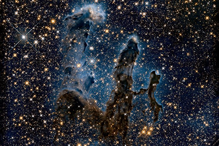 This NASA Hubble Space Telescope image, taken in near-infrared light, transforms the pillars into eerie, wispy silhouettes, which are seen against a background of myriad stars. The near-infrared light can penetrate much of the gas and dust, revealing stars behind the nebula as well as hidden away inside the pillars. Some of the gas and dust clouds are so dense that even the near-infrared light cannot penetrate them. New stars embedded in the tops of the pillars, however, are apparent as bright sources that are unseen in the visible image. The ghostly bluish haze around the dense edges of the pillars is material getting heated up by the intense ultraviolet radiation from a cluster of young, massive stars and evaporating away into space. The stellar grouping is above the pillars and cannot be seen in the image. At the top edge of the left-hand pillar, a gaseous fragment has been heated up and is flying away from the structure, underscoring the violent nature of star-forming regions. Astronomers used filters that isolate the light from newly formed stars, which are invisible in the visible-light image. At these wavelengths, astronomers are seeing through the pillars and even through the back wall of the nebula cavity and can see the next generations of stars just as they're starting to emerge from their formative nursery.