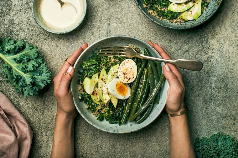 Healthy vegetarian breakfast bowls flat-lay. Quinoa, kale, green beans, avocado, egg with tahini dressing bowls over concrete background, top view. Energy boosting, clean eating, diet food concept
