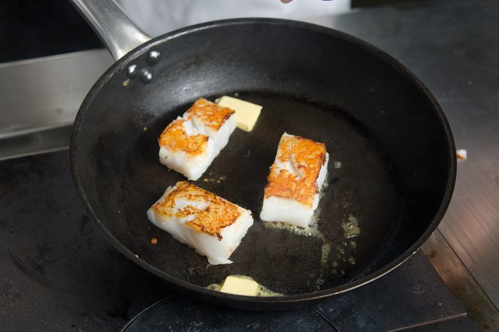 Pan fried golden fish fillet cubes, frying in real butter, in a non stick rustic pan.