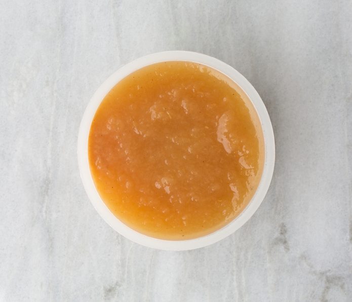 Top view of a serving of organic cinnamon applesauce in a small plastic container on a marble table.