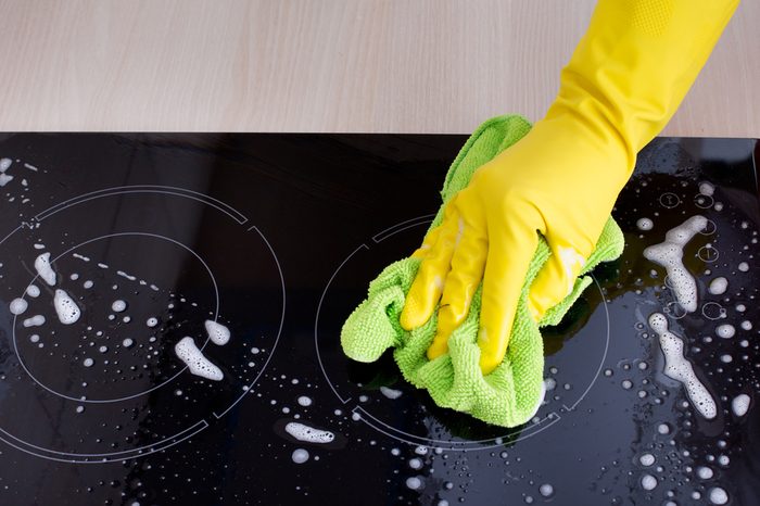 Close up of human hand with protective gloves cleaning induction hob with green mop