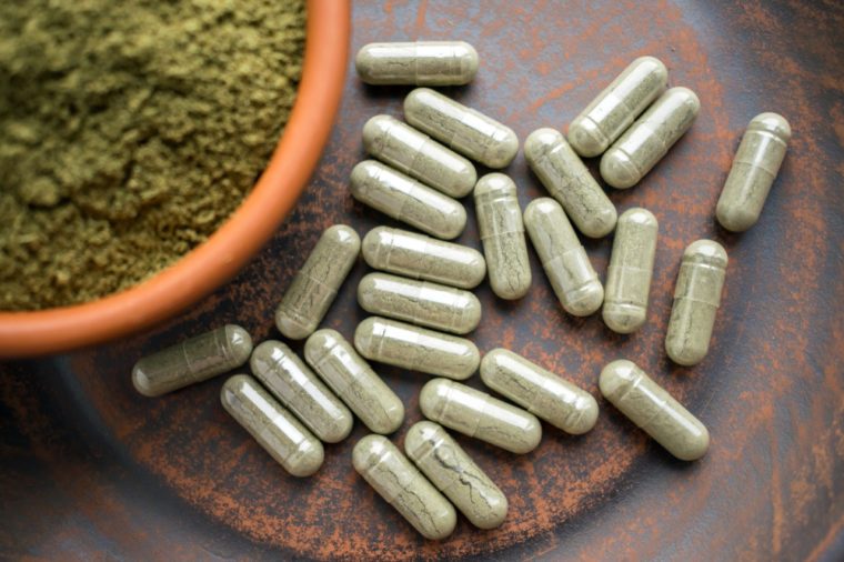 Close up Green capsules and powder on a clay brown plate on a burlap rustic background. Dietary supplements, vitamins and minerals for vegans and vegetarians. Healthy lifestyle, superfood