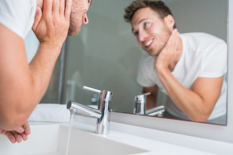 Man washing face in sink in bathroom rinsing after shaving. Home lifestyle copy space.