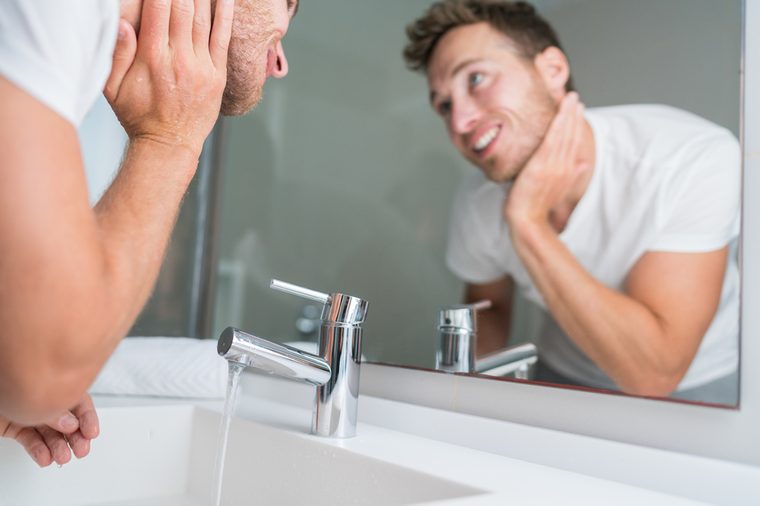 Man washing face in sink in bathroom rinsing after shaving. Home lifestyle copy space.