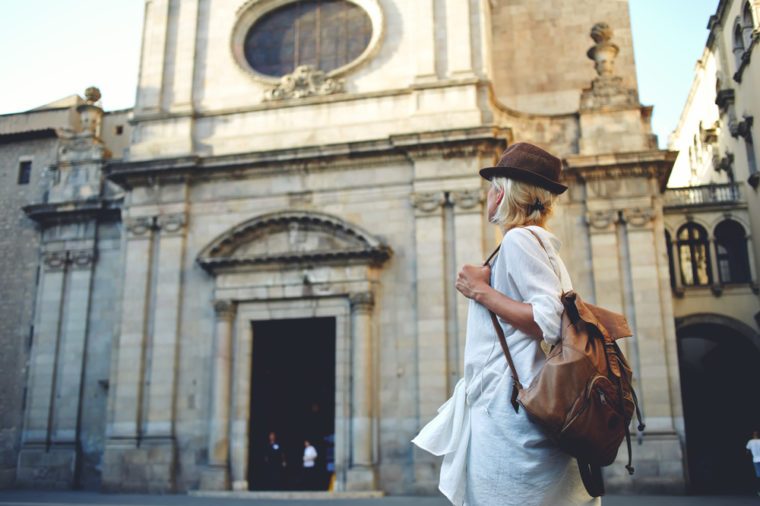 Back view of a young woman traveler with a backpack on her shoulder out sightseeing in a foreign city, stylish female foreigner examines architectural monument during her long-awaited summer vacation