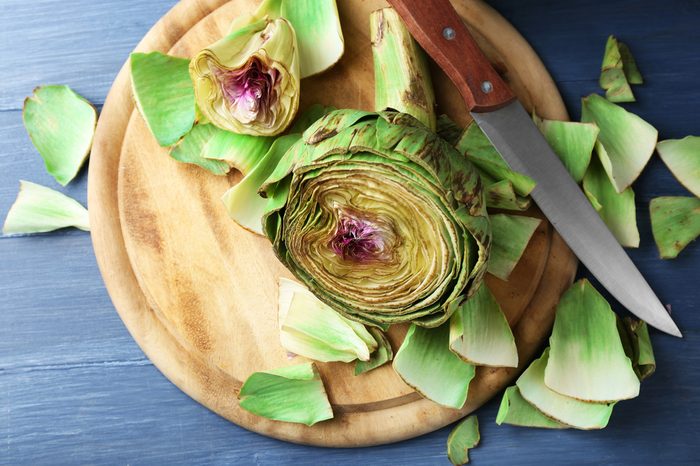 Artichokes on cutting board, on color wooden background