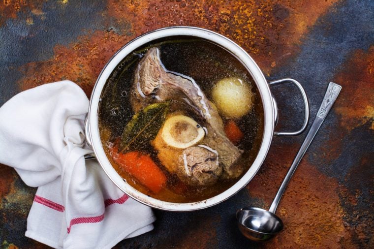 Broth soup in a cooking pot with ladle on dark stone background. Top view