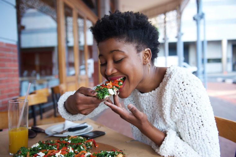 Portrait of an african american woman eating pizza at outdoor restaurant