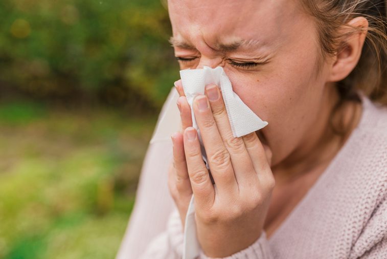 Seasonal virus infection. Sick young woman with seasonal influenza blowing her nose on a tissue. Woman has sneezing. This flu is getting to her. Young woman coughing covering her mouth with a tissue