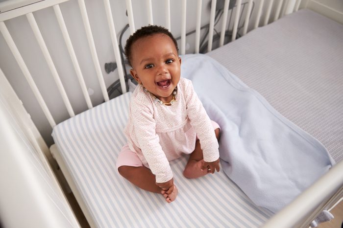 Portrait Of Happy Baby Girl Playing In Nursery Cot