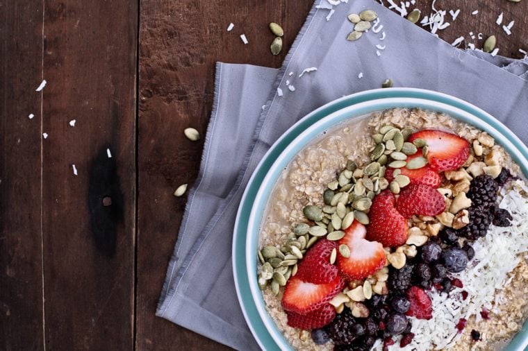 Hot breakfast of healthy oatmeal with shredded coconut, blackberries, blueberries, walnuts, heart shaped strawberries and pumpkin seeds over a rustic background. Image shot from overhead.