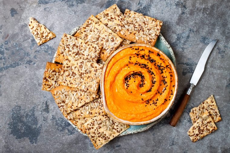 Pumpkin hummus seasoned with olive oil and black sesame seeds with whole grain crackers. Healthy vegetarian appetizer or snack 