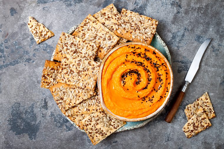 Pumpkin hummus seasoned with olive oil and black sesame seeds with whole grain crackers. Healthy vegetarian appetizer or snack 