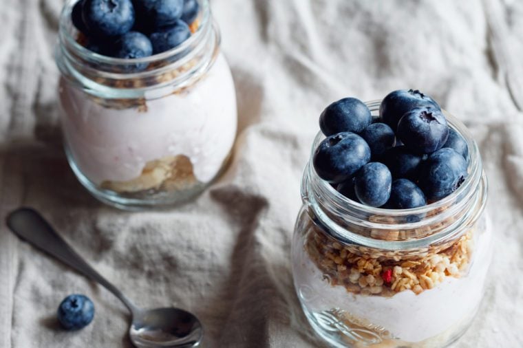 Close up of granola with fresh berries, raspberry yogurt and banana in glass jars on a rustic flax beige napkin