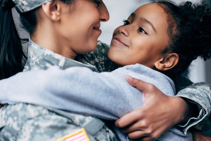 happy african american daughter hugging mother in military uniform at home
