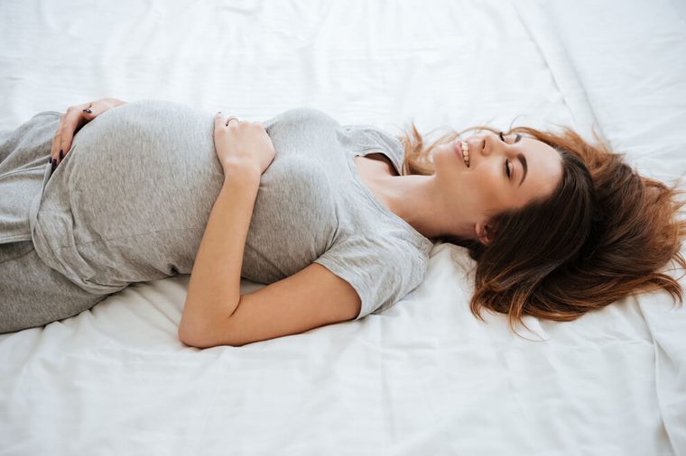 Happy pregnant young woman lying and smiling on bed at home