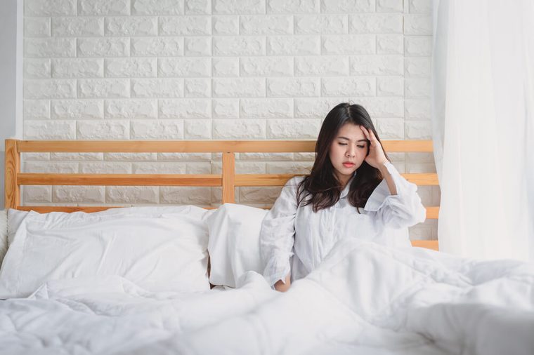 Attractive young Asian woman wake up on her bed looking unhappy and feeling sick.