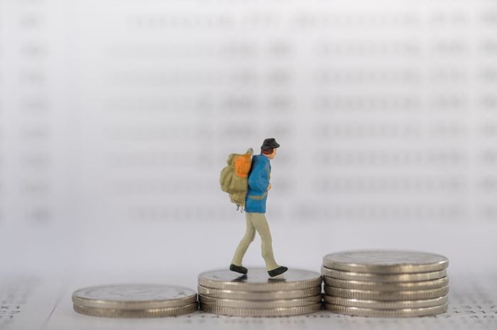 Business , travel and money concept. Traveler miniature figure with backpack walking on stack of coins on bank passbook as background.