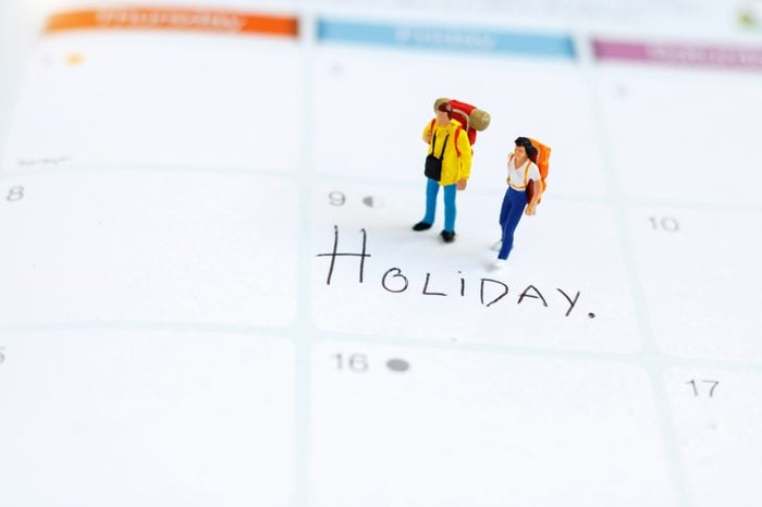 Miniature people: Backpacker standing on calendar with text "HOLIDAY". Travel on holiday and business concept.