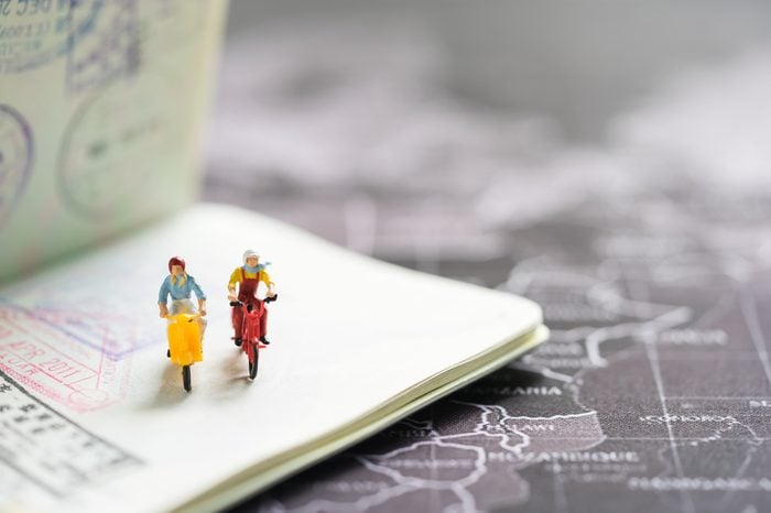 Miniature people with traveling concepts. Group of travelers riding bicycles on passport with stamps. Concept of traveling or exploring the world, budget travel