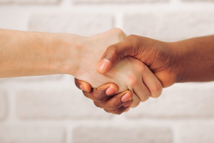 Handshake of Afro American and caucasian male hands, against white brick wall, close up