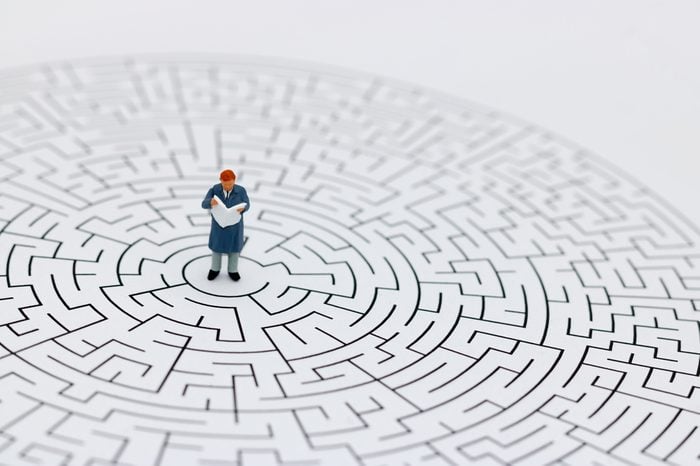Miniature people: Businessman reading on center of maze. Concepts of finding a solution, problem solving and challenge.