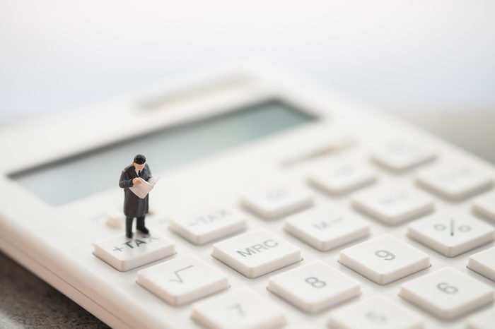 Miniature people: businessman standing on tax button of calculator. Financial, and business concept