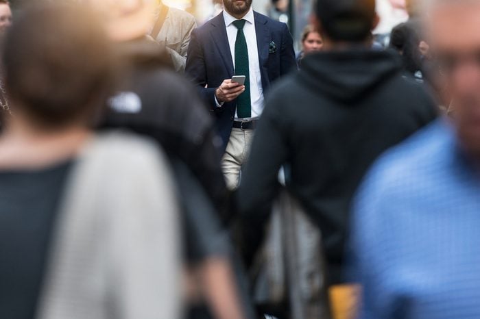 Business people walking from the job in busy city street. Elegant businessman in the people crowd walking and texting on the phone.