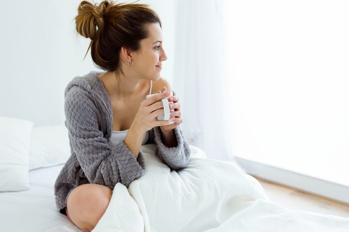 Portrait of beautiful young woman drinking coffee on bed.