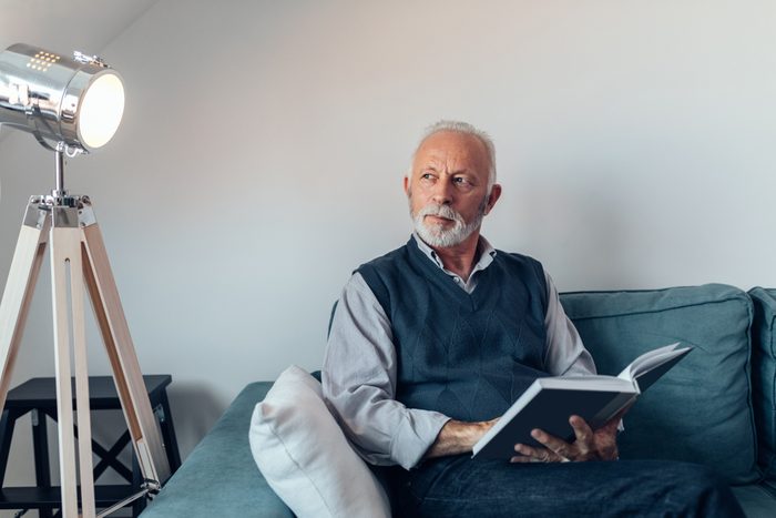 Elderly man reading a book on the sofa