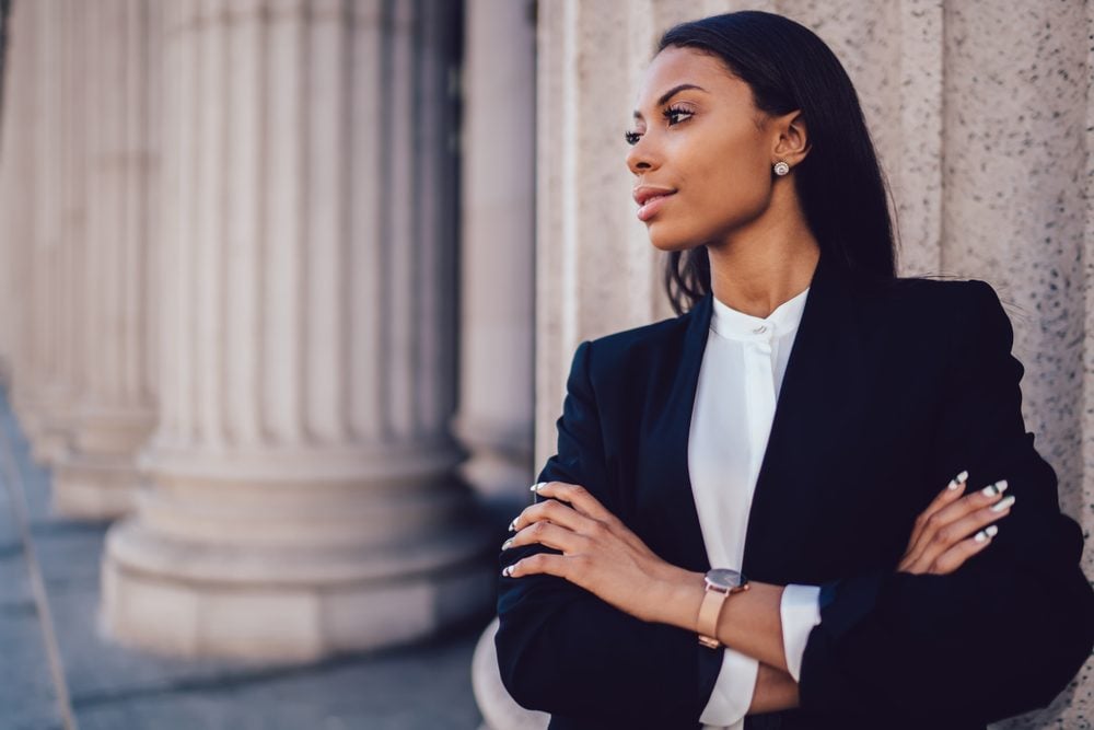 여성 아프리카 계 미국인 은행가 우아한 검은 양복을 입고 손을 접고 사무실 건물에 대해 서있는 측면을 찾고 있습니다.  교차 팔 복사 공간에 찾고 자신감 여성
기업가