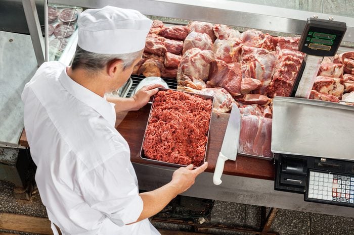 High angle view of butcher holding minced meat tray at display cabinet in butchery