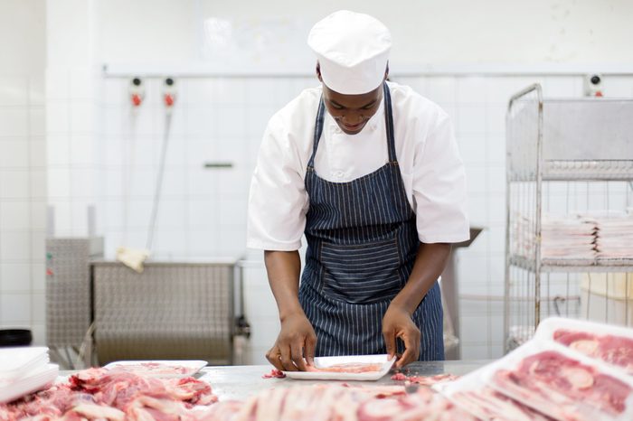 african male butcher packing meat pieces in a tray