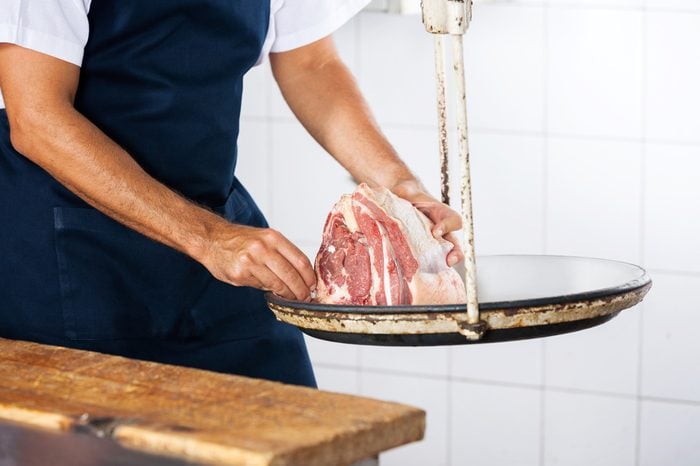 Midsection of male butcher weighing meat on scale in shop