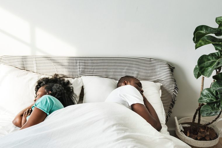 Black couple sleeping together on bed back to back