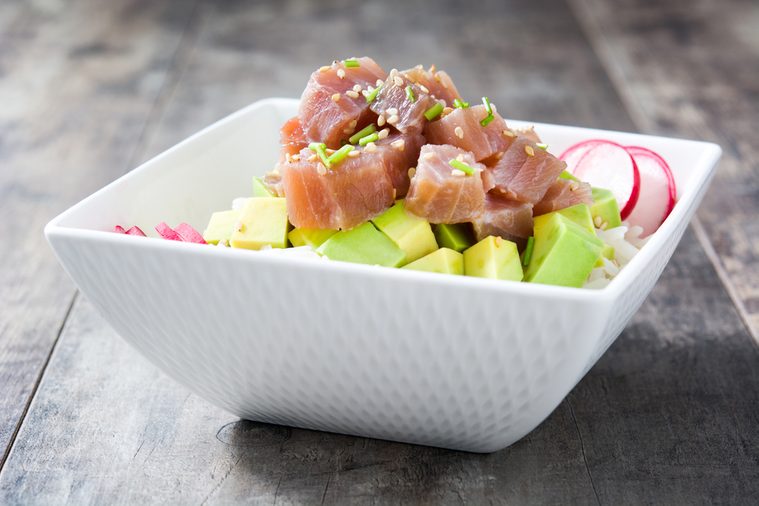 Hawaiian tuna poke bowl with avocado, radishes and sesame seeds on wooden background