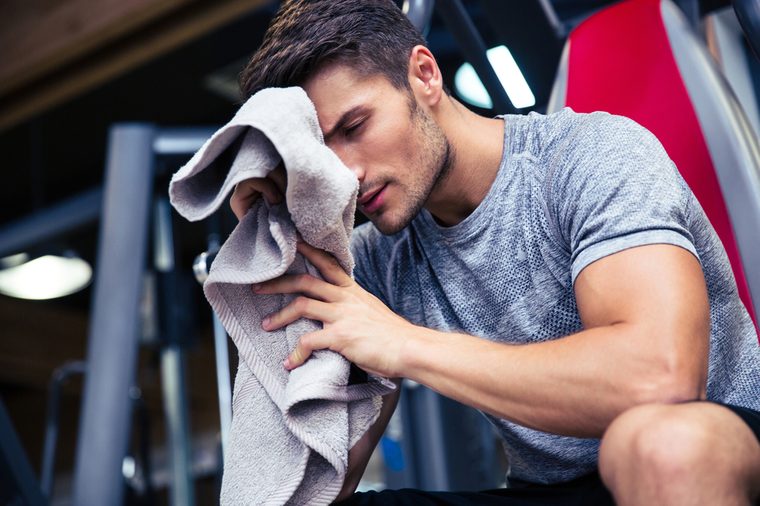 Portrait of a handsome man sitting on the bench with towel in fitness gym