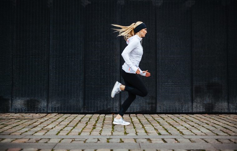 Side view of sporty young woman running on sidewalk in morning. Health conscious concept with copy space.