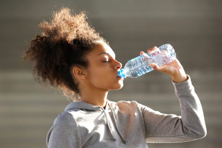 Close up portrait of an attractive young woman drinking water from bottle