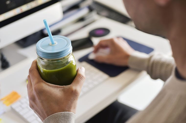closeup of a young caucasian man drinking a green detox smoothie served in a glass jar at the office