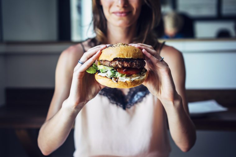 Young girl holding in female hands fast food burger, american unhealthy calories meal on background, mockup space for text message or design, hungry person smiling with grilled hamburger front view