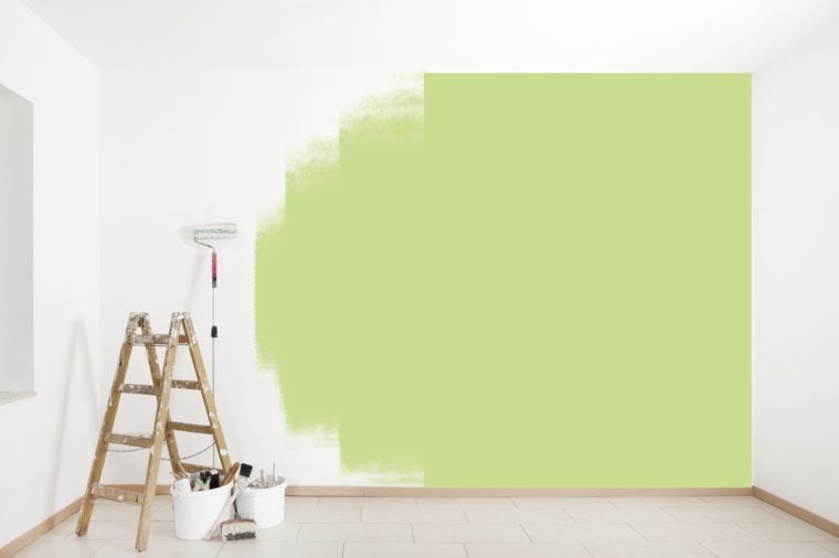 with green color is painted on a wall with ladder and painting tools