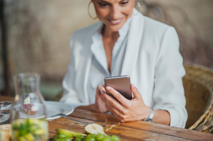 Pretty Caucasian smiling woman holding cell phone and sitting at dinner table.