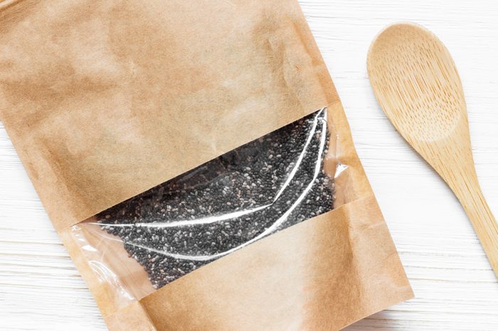 Mockup paper bag with Chia seeds and wooden spoon on white wooden table. Concept of a healthy diet. Super food. Macro