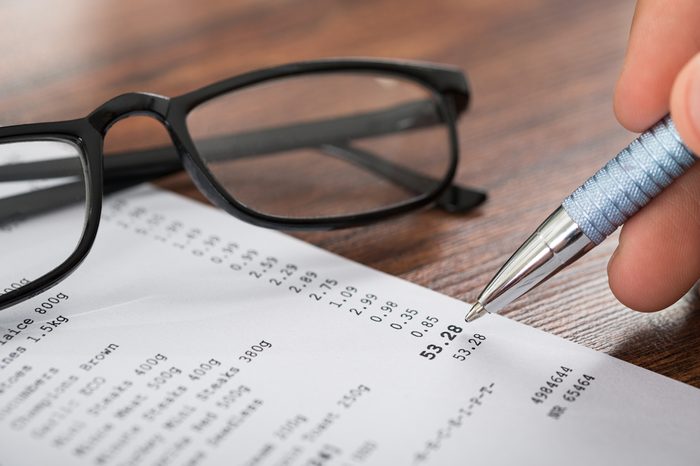 Close-up Of Person Hands Holding Pen Over Shopping Receipt And Eyeglasses