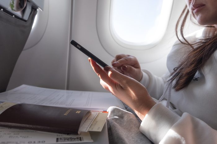 Attractive female passenger of airplane read news from networks via smartphone and wifi on board, young woman sending message on phone traveling by plane in first class connecting to wireless on phone