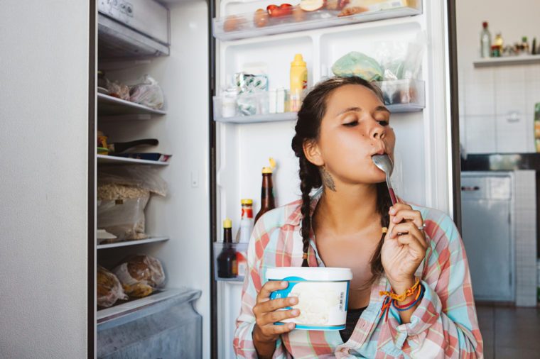 Young woman sitting next to the fridge, trying to keep diet and healthy eating. Happy to eat sweet ice cream dessert.