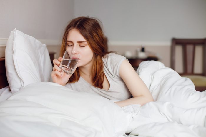 Young healthy girl drink water in her bed on morning