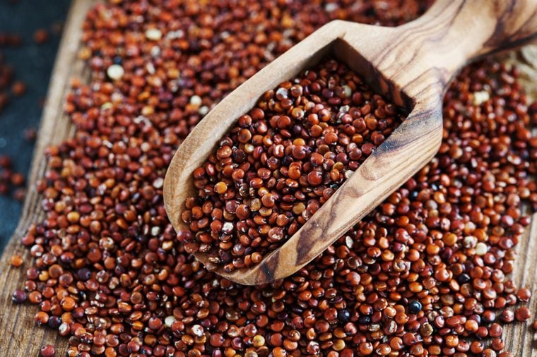 Seeds of red quinoa in wooden scoop. Chenopodium quinoa background close up, copy space